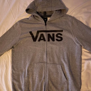 Grå hoodie från Vans med dragkedja - Säljer en grå hoodie från Vans i storlek Youth XL. Tröjan har svart Vans-logga framtill, dragkedja hela vägen, huva och två fickor. Tillverkad i mjuk bomullsblandning, perfekt för chill dagar. Klassisk streetwear-stil med lång ärm och relaxed fit. 399kr Nypris! 