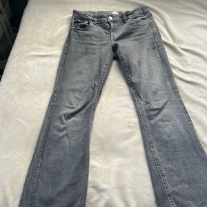 Grå bootcut jeans från Gina Tricot - Snygga grå jeans från Gina Tricot med bootcut passform. Jeansen har broderade detaljer på bakfickorna och dekorativa knappar. Tillverkade i mjukt denimtyg som sitter skönt hela dagen.