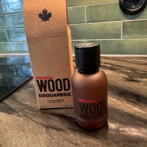 DSQUARED2 Wood Eau de Parfum 50ml - DSQUARED2 Wood Original Eau de Parfum, 50 ml. Flaskan är mattbrun med svart kork och tydlig logga. Kommer i en stilren kartong i naturfärgat papper med svart och röd text. En parfym med träig och fräsch vibe, perfekt för dig som gillar unika dofter.