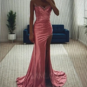 Rosa balklänning - Supersnygg rosa långklänning i glansigt satinliknande material. Klänningen har genomskinliga axelband med figurnära passform, v-ringad urringning och hög slits framtill. Dekorativa detaljer med glittrande pärlor längs urringning och slits. Perfekt för bal eller fest! Endast använd 1 gång (inga täcken på användning)