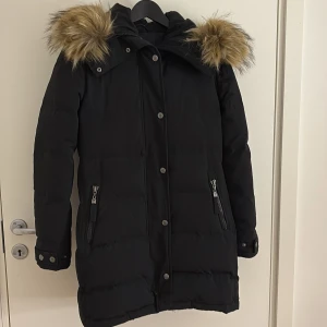 Svart vinterjacka från hollies ”subway” - Svart vinterjacka från Hollies med stor huva och fluffig päls. Jackan har dragkedja, knappar och två fickor med dragkedja framtill. Perfekt för kalla dagar med sin långa modell och sitt tjocka material. Badge på ärmen och justerbara ärmslut. Hade den ett par gånger förra vintern, hade inte någon stor använding av den då jag hade andra jackor jag valde att ha på mig. Klassas nog nästan som ny utan prislapp. Jätte fräsch. Köpt för 4000kr, kontakta vid frågor och funderingar kring varan och priset❣️