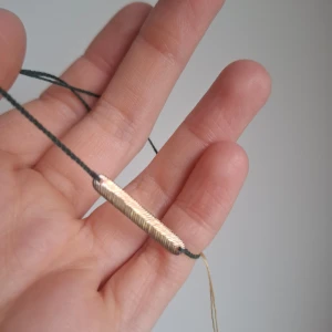 Armband från Anna + Nina med silverfjäder - Unikt armband från Anna + Nina med en avlång, räfflad silverfärgad fjäder på mörkgrön tvinnad tråd. Armbandet har små tofsar i ändarna och minimalistisk design som ger en cool och stilren vibe.