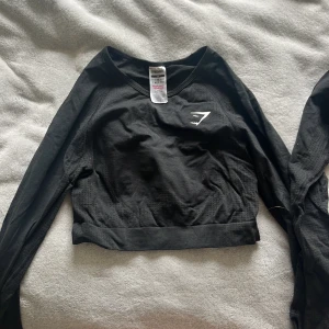 Svart croppad långärmad tröja Gymshark - Säljer en eller två svarta croppade långärmade tröjor från Gymshark i storlek M. Tröjan har en tight passform, diskret Gymshark-logga på bröstet och är tillverkad i ett stretchigt material av nylon och elastan. Perfekt för träning och sportiga outfits. Säljer en för 145 och två för 245! En av dem har ett litet hål i armhålan som knappt syns, se bild. Köpte dem för 350kr/st.