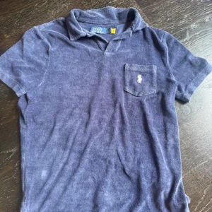 Marinblå frotté polo från Ralph Lauren - Snygg marinblå polo t-shirt från Ralph Lauren med klassisk krage och bröstficka med broderad logga, perfekt för en chill och stilren look.