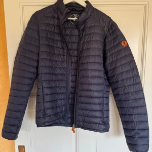 Mörkblå Save the duck jacka  - Snygg mörkblå jacka från Save the duck me diskret logga på ärmen. Säljer den då den tyvärr har blevit för liten för mig samt bara hänger i garderoben. Små i storleken så skulle säga L passar m bättre. Perfekt för kyliga dagar när du vill hålla stilen enkel och clean.