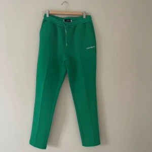 Gröna mjukisbyxor från Les Deux - Snygga gröna mjukisbyxor från Les Deux med vit logga på låret. Byxorna har dragsko i midjan och raka ben med markerad pressveck. Perfekta för en chill och sportig stil.