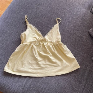 Ljusgul linnetopp med spetsdetalj - Supersöt ljusgul linnetopp med tunna axelband och v-ringning. Toppen har en feminin spetskant längs urringningen och en lätt rynkad söm under bysten som ger en avslappnad passform. Perfekt för varma dagar och enkel att styla till olika looks. Nypris 450 kr därför säljer jag den för 350, den har bara använts 1-2 gånger. 