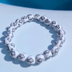 Vitt pärlarmband med korsmönster - Coolt armband med vita runda pärlor och svarta kors på varje pärla. Perfekt accessoar för dig som gillar unika detaljer och vill sticka ut lite extra. Elastiskt band gör det enkelt att ta på och av. Passar yngre barn Nytt