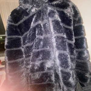 Svart pälsjacka med huva - Säljer en svart pälsjacka med huva och rutigt mönster. Jackan är fluffig och har en riktigt mjuk känsla, perfekt för kalla dagar. Oversized fit för en chill vibe. Passar dig som vill sticka ut och hålla dig varm samtidigt.