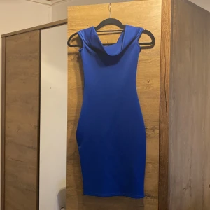 Kornblå tight klänning från Club L - Säljer en kornblå, tight och ärmlös klänning från Club L i storlek XS. Klänningen är kort, har en snygg draperad halsringning och dragkedja i sidan. Materialet är stretchigt och följsamt, perfekt för dig som vill sticka ut med färg.