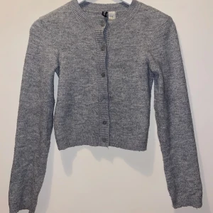 Grå kofta från H&M DIVIDED XXS - Mysig grå kofta från H&M DIVIDED i storlek XXS. Den är stickad med ribbade muddar och knappar framtill. Perfekt för lager-på-lager och har en klassisk rund halsringning. Enkel att matcha med allt i garderoben.