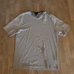 Beige t-shirt från H&M med textdetalj - Beige t-shirt från H&M i relaxed fit med svart texten 'TRANQUILITY' runt halsringningen. Klassisk modell med korta ärmar och rund hals. Tillverkad i mjuk bomull.
