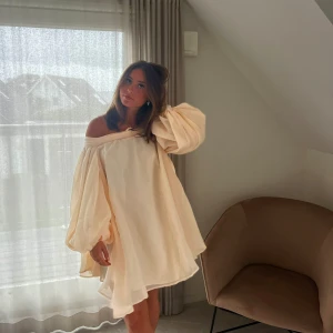 Beige klänning med rosett - Flowy klänning. Beige off shoulder. Rosett i ryggen. Passar allt från XS till M det beror på hur hårt man knyter rosetten. 