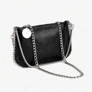 Svart axelväska med kedja - Snygg svart axelväska i skinn med silverfärgade kedjor och dragkedja. Väskan har en cool detalj med rund metallbricka och dekorativa sömmar längs kanterna. Perfekt storlek för det viktigaste och ger en edgy vibe till din outfit.