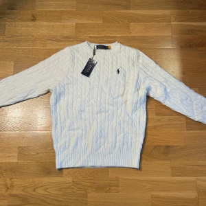 Vit kabelstickad tröja Polo Ralph Lauren - Säljer en klassisk vit kabelstickad tröja från Polo Ralph Lauren. Tröjan har rund halsringning, lång ärm och den ikoniska broderade loggan på bröstet. Perfekt för dig som gillar en clean och tidlös stil. Den är M men passar XS/S