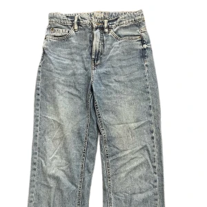Blå raka jeans i vintage-stil - Klassiska blå jeans med rak passform. Jeansen har en ljus tvätt och tydliga slitningar för en avslappnad vintage-look. Tillverkade i bomull med synliga sömmar och bälteshällor. Perfekta för dig som gillar en tidlös och chill stil.