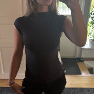 Mörkgrå ärmlös topp från Gina Tricot - En mörkgrå, tight och stilren topp från Gina Tricot i storlek S. Toppen är ärmlös med hög hals och har en enkel, clean look som passar till allt. Tillverkad i mjuk bomull som känns skön mot huden. .