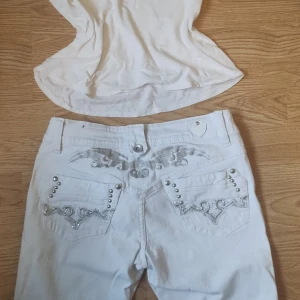 Vita jeansbyxor med silvriga detaljer - Säljer ett par vita jeansbyxor från en säljare på Vinted men jag säljer de pga att de är för små då jag är M. De är 1/3 jeans med silvriga broderier och nitar på bakfickorna och ovanför fickorna. Byxorna har snygga detaljer i form av mönster och blanka nitar.