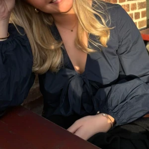 Mörkblå omlottblus från Nelly - Supersnygg mörkblå omlottblus från Nelly med croppad passform och långa puffiga ärmar. Djup v-ringning och knyt framtill ger en trendig look. Perfekt att styla med höga jeans eller kjol för en cool vibe.