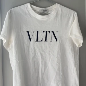 Vit t-shirt från Valentino - Säljer en stilren vit t-shirt från Valentino med VLTN-tryck i svart på framsidan. T-shirten är kortärmad och har en klassisk rund halsringning. Perfekt för en avslappnad och trendig look.
