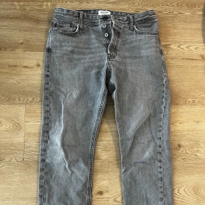Grå jeans från Jack & Jones - Snygga grå jeans från Jack & Jones med en klassisk femficksdesign. De har en knappgylf och är tillverkade i ett slitstarkt material. Perfekta för en avslappnad stil.