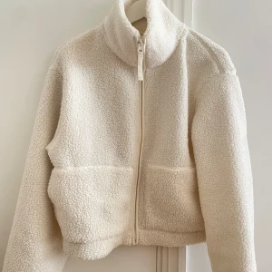 Vit teddyjacka med dragkedja - Mysig vit teddyjacka med dragkedja framtill från H&M. Jackan har en hög krage och två stora fickor framtill. Använd fåtal gånger. Strl M. Inga sminkfläckar. 