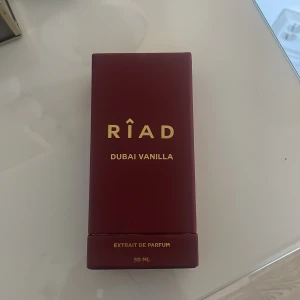 Riad Dubai Vanilla Extrait de Parfum - Upptäck Riad Dubai Vanilla, en lyxig Extrait de Parfum i en elegant frostad glasflaska med gyllene detaljer. Denna doft erbjuder en rik och sensuell vaniljarom, perfekt för den som älskar orientaliska toner. Flaskan rymmer 50 ml och kommer i en stilren vinröd förpackning med guldtext. Öppnad och bara använt ca 1 gång. Kvitto finns på mail.