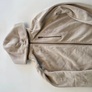 Beige huvtröja med dragkedja - Säljer en stilren beige huvtröja från Sail racing. Tröjan har en dragkedja framtill och en praktisk huva. Perfekt för en avslappnad stil.