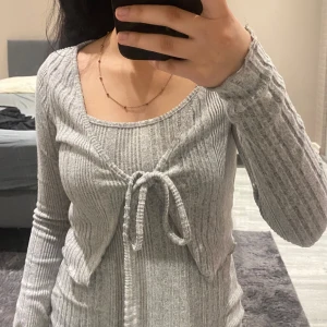 Grå ribbad klänning med kort kofta  - Snygg grå ribbad klänning med smala axelband och en matchande långärmad kofta med knytband framtill. Perfekt för en stilren och bekväm look.