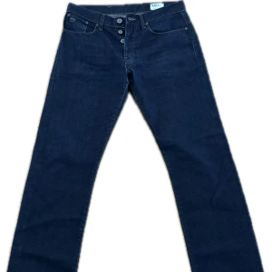 Mörkblå jeans från G-Star - Säljer ett par mörkblå jeans från G-Star med knappgylf och klassisk femficksdesign. Modellen är 3301 Straight, vilket ger en rak passform. Perfekta för en stilren look.