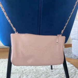 Rosa axelväska från Zadig & Voltaire - Jättesnygg rosa axelväska från Zadig & Voltaire med texten 'Girls Can Do Anything' präglad på framsidan. Väskan har en silverfärgad kedjerem och en praktisk dragkedja på baksidan för extra förvaring. Perfekt för att bära med sig det viktigaste med stil. 2 olika fack och båda har dragkedja ett större fack och ett mindre på baksidan helt. Aldrig använt väskan ute
