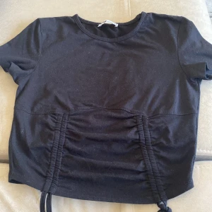 Svart kortärmad topp med snörning - Snygg svart kortärmad topp med snörningsdetaljer framtill. Perfekt för en stilren look.