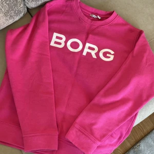 Rosa tröja från Björn Borg - Säljer en snygg rosa tröja från Björn Borg med stort tryck på framsidan. Tröjan har långa ärmar och en klassisk rund halsringning. Perfekt för en färgglad och bekväm stil. 💖