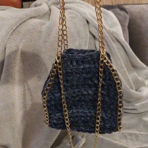  Blå virkad väska med guldkedja - Snygg blå virkad väska i mörkgrått med en elegant guldkedja. Perfekt för att ge en stilfull touch till din outfit. Väskan har en unik textur och är både praktisk och trendig.