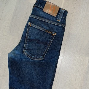 Mörkblå jeans från Nudie Jeans - Säljer ett par mörkblå jeans från Nudie Jeans då de inte passar mig längre. Det finns ett litet märke(Se bild 5) som man inte ser när man har på sig dom och ett hål på insidan av vänster ficka. Hör av dig vid funderingar. Priser är inte helt hugget i sten.