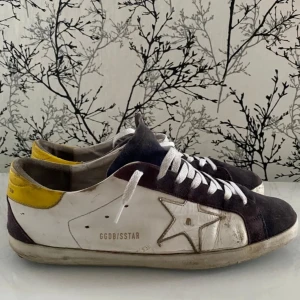 Golden Goose sneakers med stjärndetalj - Snygga sneakers från Golden Goose i en cool kombination av vitt, gult och mörkbrunt. Skorna har en ikonisk stjärndetalj på sidan och är tillverkade i skinn och mocka. Perfekta för en avslappnad stil med en touch av lyx.