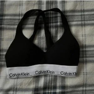 Svart linnetopp från Calvin Klein - Säljer en stilren svart linnetopp från Calvin Klein med vit resårkant och logga. Perfekt för en avslappnad look eller som underkläder. Toppen har en enkel och bekväm design.