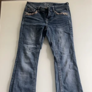 Grace in LA - Snygga blå jeans med unika broderade detaljer på fickorna och bakfickorna. De har en bootcut-stil och låg midja, vilket ger en avslappnad och trendig look. Perfekta för dig som vill ha något extra i din garderob.