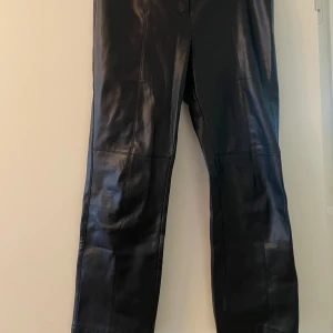 Svarta skinnbyxor från Sfera - Snygga svarta skinnbyxor från Sfera med en stilren design. Byxorna har en knapp framtill och är perfekta för en trendig look. Passar bra till både vardag och speciella tillfällen.