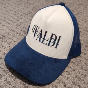 Blå och vit keps från BVALDI - Snygg keps från BVALDI i blått och vitt med broderad logga framtill. Kepsen har ett justerbart spänne bak och meshmaterial för extra ventilation. Perfekt för en avslappnad stil.