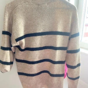 Beige och svart randig tröja - Säljer en beige tröja med svarta ränder. Tröjan har långa ärmar och en rund halsringning. Perfekt för kyligare dagar.