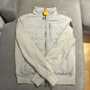 Parajumper Cardigan - Säljer en stilren grå cardigan Parajumpers. Jackan kombinerar fleece med en dragkedja framtill och en broderad logga på ärmen. Perfekt för kyligare dagar med sin quiltade stil och praktiska fickor. Pris går att diskutera! Relativt ny med inga skador