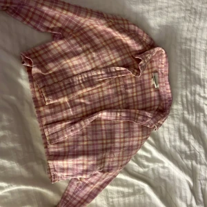 Rutig rosa skjorta från Monki - Säljer en söt rutig skjorta från Monki i rosa och vita nyanser. Skjortan har en avslappnad passform med långa ärmar och en klassisk krage. Perfekt för en casual look.