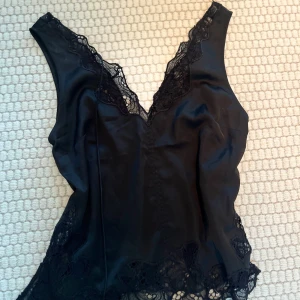 Svart linne med spetsdetaljer - Elegant svart linne med v-ringad spetskant och spetsdetaljer längs nederkanten. Perfekt för en stilren look.