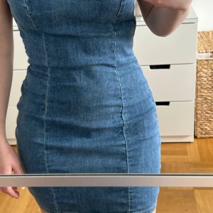 Blå jeansklänning - Snygg blå jeansklänning med smala axelband och en tight passform. Perfekt för en avslappnad men stilren look. Klänningen har en dragkedja i ryggen för enkel på- och avtagning.