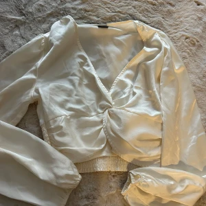 Vit omlottblus från Gina Tricot - Superfin vit omlottblus från Gina Tricot i storlek 36. Blusen har långa puffiga ärmar med resår vid handlederna, v-ringning och snygg twistad detalj framtill. 