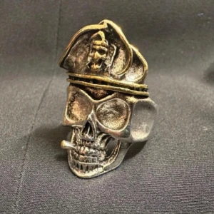 Dödskallering med cigarett & kaptenshatt - Justerbar storlek- Nyskick  -  Tung och detaljrik ring i stål/metallegering med dödskalle, kaptenshatt och cigarett – en accessoar med attityd för dig med alternativ stil. Silver- och guldfärgad finish med rå känsla. Justerbar storlek som passar de flesta. Höjd ca 3,5 cm. Perfekt till punk, rock eller goth. Priset är redan lågt, så jag prutar inte – men jag erbjuder bundlerabatt. Jag rensar garderoben – kolla gärna mina andra annonser också! 