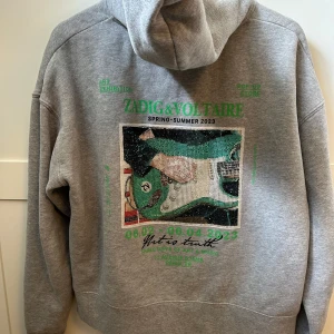 Grå hoodie Zadig & Voltaire med print - Grå limited edition hoodie från Zadig & Voltaire med coolt print och glittriga stenar på ryggen. Jättebra skick, nypris 3500kr. Kan tänka mig att diskutera priset!