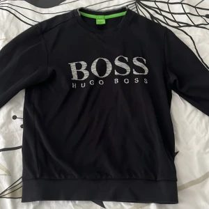 Svart Hugo Boss sweatshirt slim fit S - Svart sweatshirt från Hugo Boss i slim fit med stort BOSS-tryck i vitt och grått framtill. Klassisk rund halsringning och långa ärmar. Perfekt för dig som gillar stilrena och snygga loggoplagg.