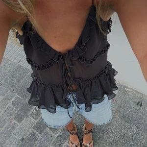 Svart volangig linnetopp från Zara - Supersöt svart linnetopp från Zara med volanger och snörning framtill. Tunt, lätt material som ger en luftig känsla. Djup v-ringning och smala axelband, perfekt för varma dagar eller när du vill känna dig extra stylish.